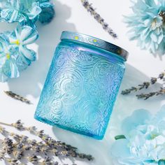 a blue glass jar sitting on top of a table next to flowers and lavenders