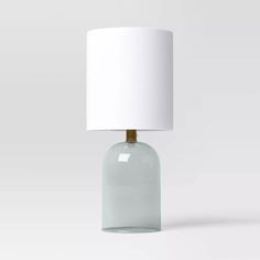 a glass table lamp with a white shade on the base and a light bulb attached to it