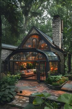 a house in the woods with lots of windows and plants on the front porch, surrounded by greenery