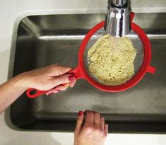 a person is grating something in a red strainer on the sink with their hands