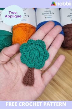 crochet flower in the palm of someone's hand with four balls of yarn behind it