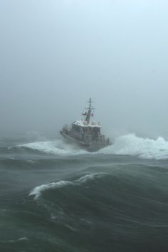 a large boat in the middle of some rough ocean water on a foggy day