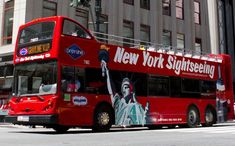 a red double decker bus driving down a street next to tall buildings and traffic lights