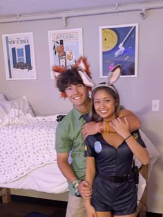 a man and woman standing next to each other in front of a bed with posters on the wall