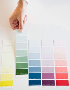 a hand is holding a color swatch over a white table with several colors on it