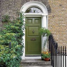 a green door is on the side of a brick building with potted plants next to it