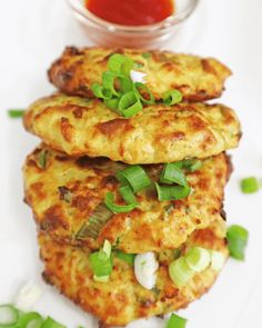 three fritters on a plate with sauce and green onions