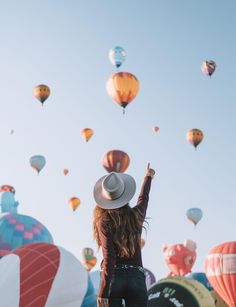 a woman standing in front of many hot air balloons flying through the sky with her arms up