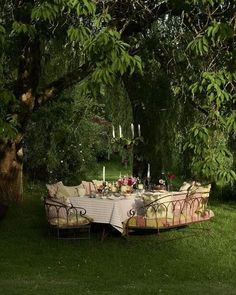 an outdoor dining table set up in the grass under a tree with candles and flowers on it