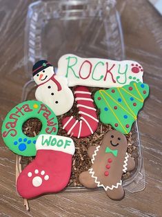 decorated christmas cookies in a clear box on a wooden table with the word rocky spelled out