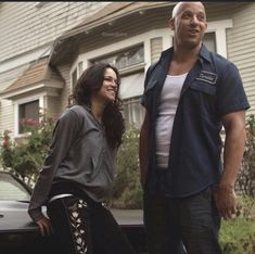 two people standing next to a car in front of a house