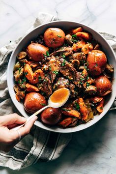 a person holding a spoon in a bowl filled with potatoes and meat on a table