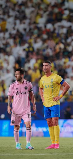 two soccer players standing on the field during a game with spectators in the stands behind them