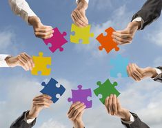 several people holding puzzle pieces together in the shape of a circle against a blue sky