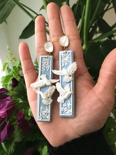 a hand holding two earrings with birds on them