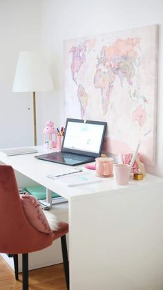 a laptop computer sitting on top of a white desk next to a pink chair and lamp