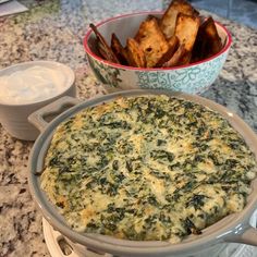 a casserole dish with spinach and cheese on the side next to some dipping sauce