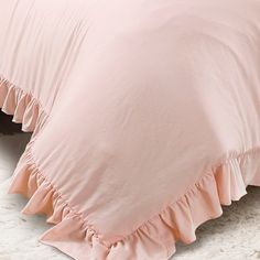 a pink bed with ruffles on it and a white rug in the background