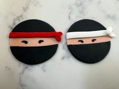 two cookies decorated to look like ninjas are on a marble counter top, one is black and the other is red