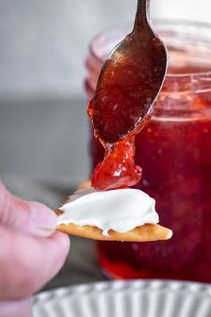 a spoon full of jelly is being held over a plate with cookies and jam in the background