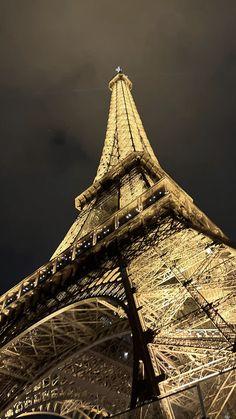 the eiffel tower lit up at night with dark clouds in the sky behind it