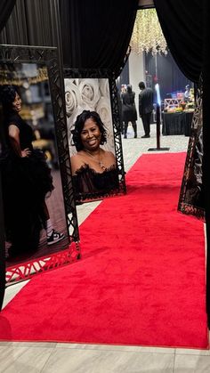 a red carpeted area with black curtains and pictures on the walls, in front of a chandelier