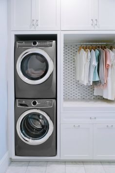 a washer and dryer sitting in front of white cabinets with clothes hanging on them