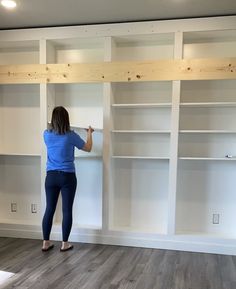 a woman standing in front of some white bookshelves with wooden shelves on each side