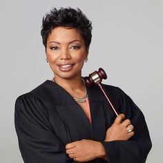 a woman holding a judge's hammer in her right hand and smiling at the camera