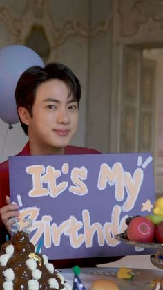 a boy holding up a sign that says it's my birthday with fruit and balloons in the background