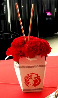 red flowers in a white container on top of a table with silverware and utensils