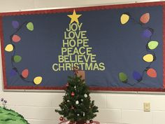 a decorated christmas tree in front of a bulletin board that says joy love hope peace believe christmas