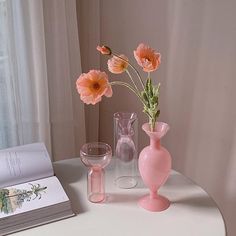 three vases with flowers in them on a table next to a book and wine glass