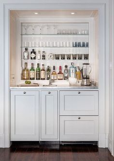 a white kitchen with lots of bottles on the counter and shelves in front of it