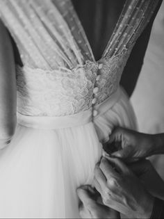 black and white photograph of woman tying dress on bride's wedding day, close up