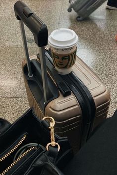 a coffee cup sitting on top of a piece of luggage next to a handbag