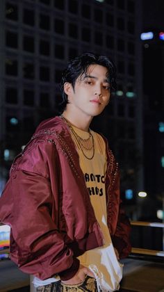 a young man standing in front of a tall building wearing a maroon jacket and white pants