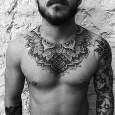 a shirtless man with tattoos on his chest and shoulder is standing in front of a white wall