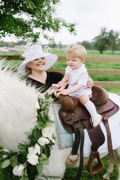 a woman holding a baby riding on the back of a white horse