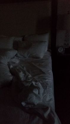 an unmade bed with white sheets and pillows in a dark room at night time