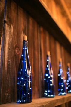 blue bottles are lined up on a wooden shelf with lights in the backround