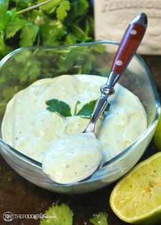 a glass bowl filled with sauce and garnished with cilantro next to limes