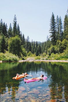 two people are floating on their stomachs in the water near some rocks and trees