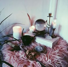 a table topped with candles and other items on top of a fur covered floor next to a wall