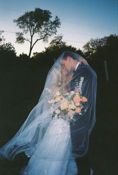 a bride and groom kissing under a veil in front of the setting sun at their wedding