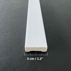 a long white piece of plastic sitting on top of a black floor next to a ruler