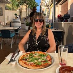 a woman sitting at a table in front of a pizza with toppings on it