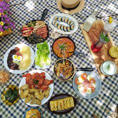 a table topped with plates and bowls filled with food next to utensils on top of a checkered cloth