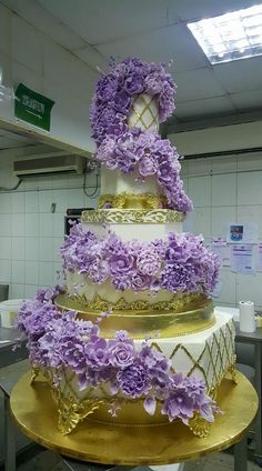 a three tiered cake with purple flowers on the bottom and gold trimmings