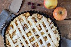 an apple pie sitting on top of a wooden table next to two apples and a knife